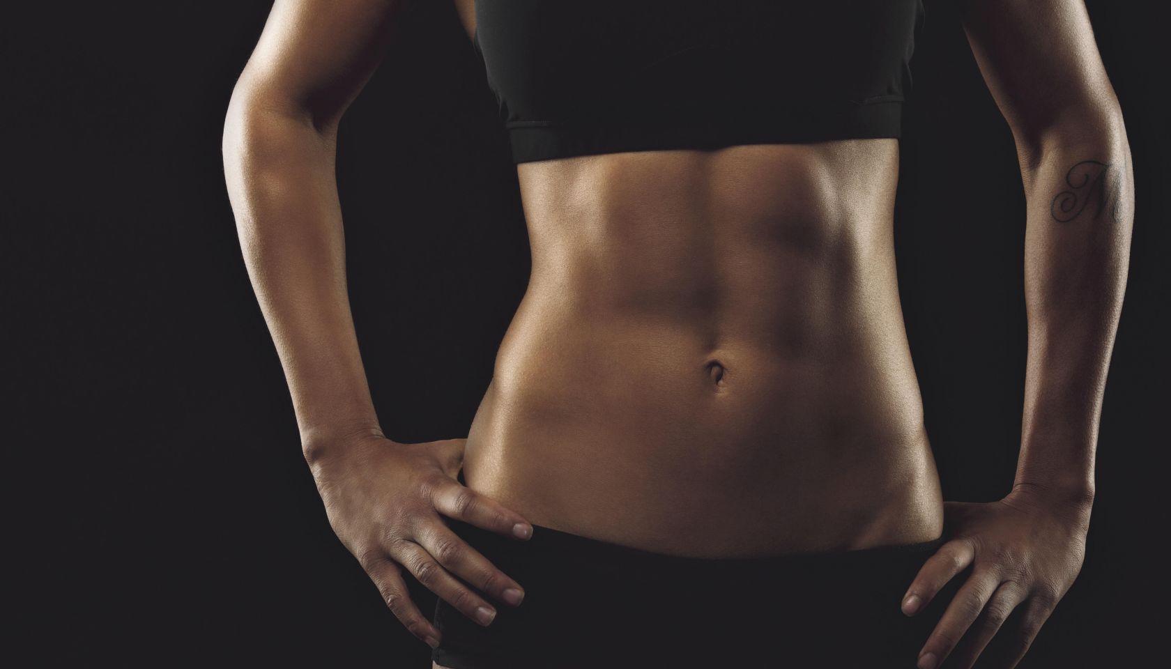 Close up of fit woman's torso with her hands on hips. Female with perfect abdomen muscles on black background