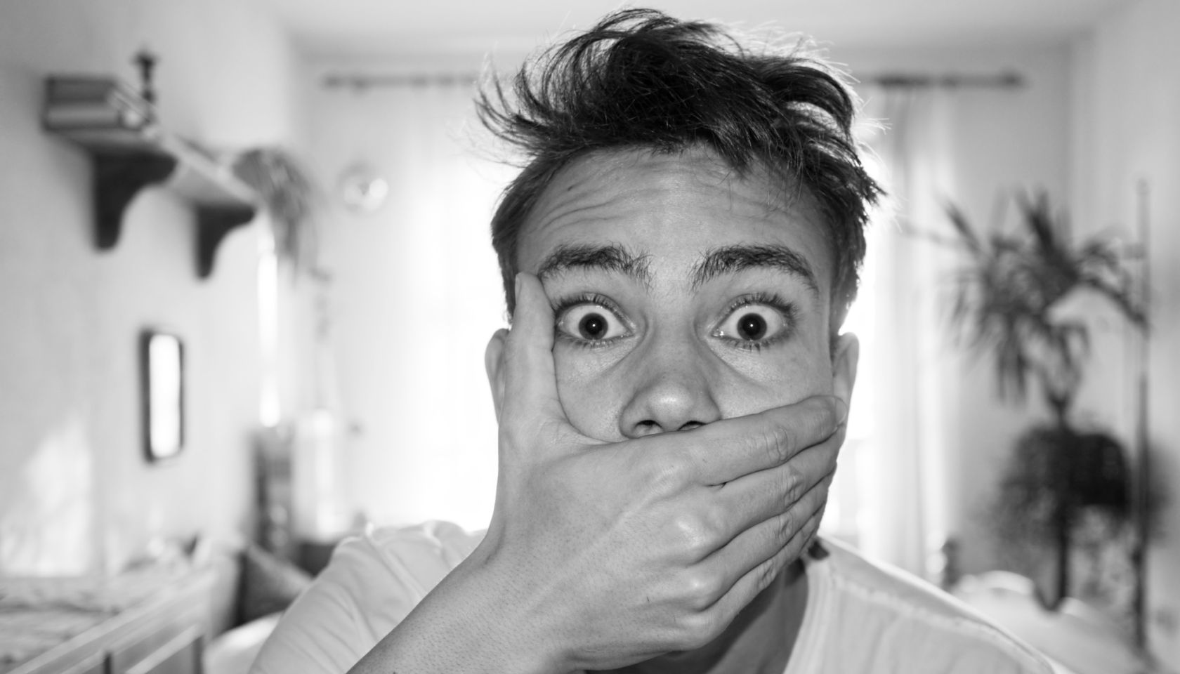 Portrait Of Shocked Man Covering Mouth At Home