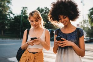 Two friends together in the city with mobile phone at sunset