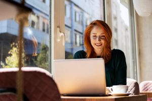 Redhead Woman Working On Laptop In The Morning And Enjoying Coffee