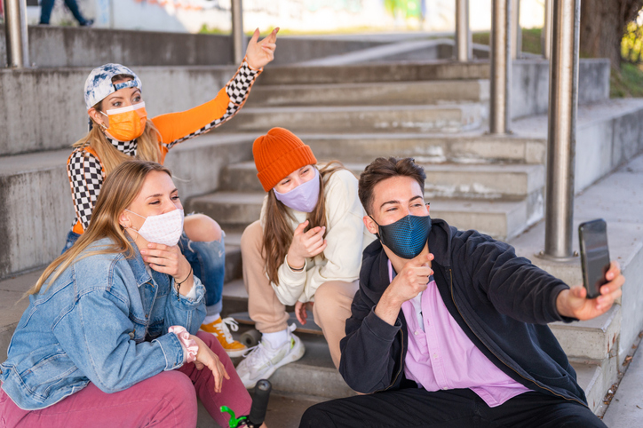 Young friends protected with face masks sitting outdoors with skateboards and bmx bicycle